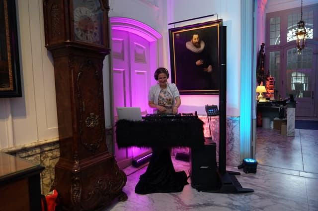 DJ achter de draaitafel in een monumentale ruimte met roze en blauwe sfeerverlichting
