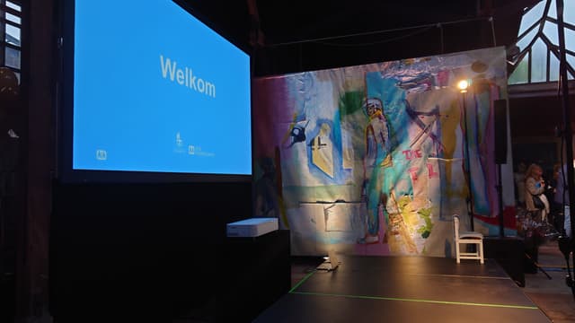 Groot projectiescherm met short-throwbeamer naast een kleurrijk kunstwerk