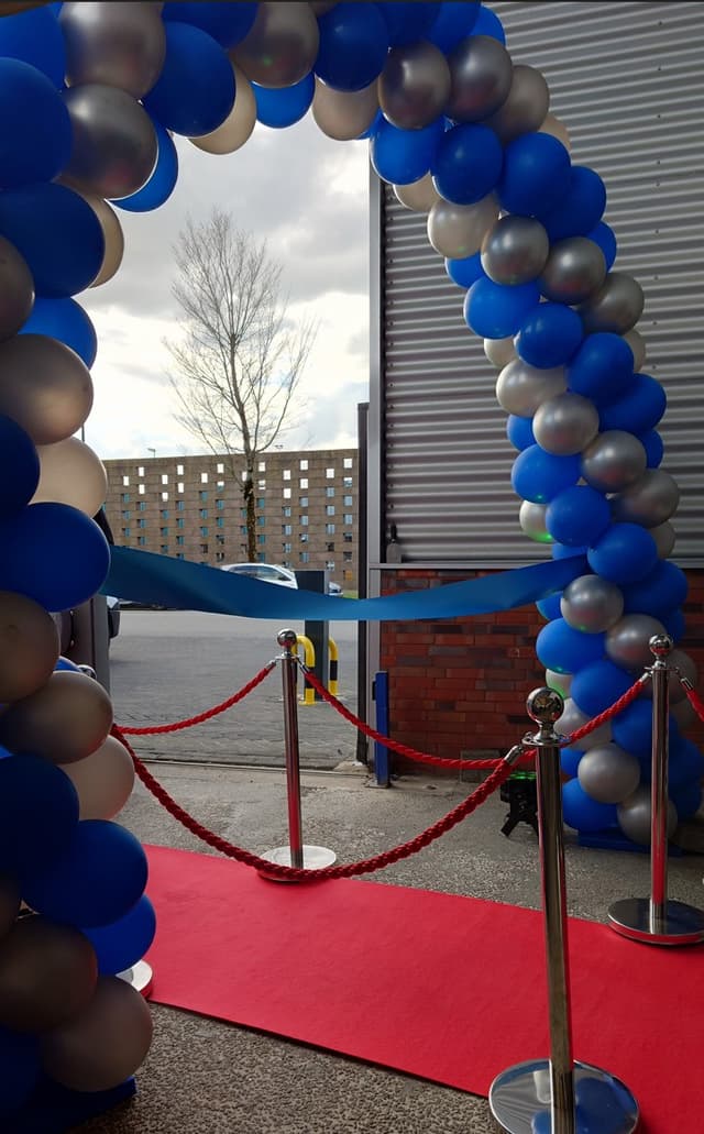 Rode loper met chrome afzetpaaltjes en rode koorden bij een entree met ballonboog